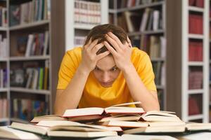 Tired caucasian guy holding head and reading book, getting ready for exams photo