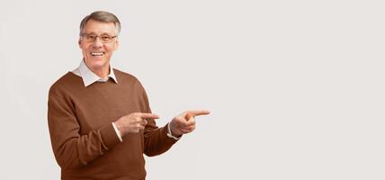 Look There. Cheerful Elderly Man Pointing Fingers Aside At Copy Space Standing Over White Studio Background. Panorama photo