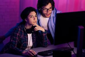 A young couple is engrossed in a game, the man standing behind the woman, both wearing headsets and focused on the computer monitor in front of them. photo