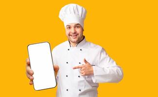 Positive Chef Man Pointing Finger Showing Empty White Board In His Hands Standing Over Yellow Studio Background. Mockup photo