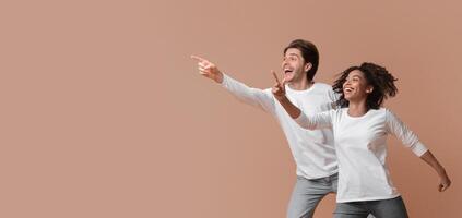 Cool offer. Joyful multiracial couple pointing at copy space and jumping over yellow background in studio, full length shot photo