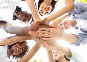 Student Friendship. Portrait of happy university friends stacking hands together, showing unity and togetherness, low angle view, selective focus photo