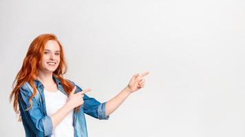 A woman with vibrant red hair is pointing decisively at an unseen object or location, copy space on plain background, panorama photo
