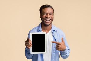 African American Man Pointing Finger At Blank Tablet Screen Smiling At Camera Standing On Yellow Background. Studio Shot, Mockup photo