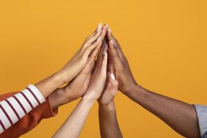 The image showcases multiple hands of various skin tones reaching upwards and touching in a gesture of unity and collaboration, cropped photo
