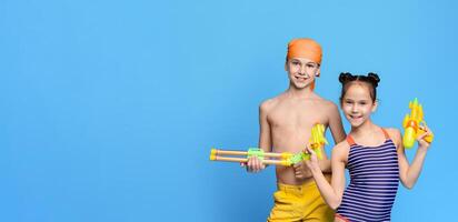 Two cheerful children, dressed in bright swimwear and headbands, are smiling while holding colorful water guns, ready for some fun activities, panorama with copy space photo