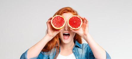 A woman is holding two grapefruits up to her eyes, covering them completely. She appears to be looking through the grapefruits, creating a funny and quirky visual effect, web-banner photo