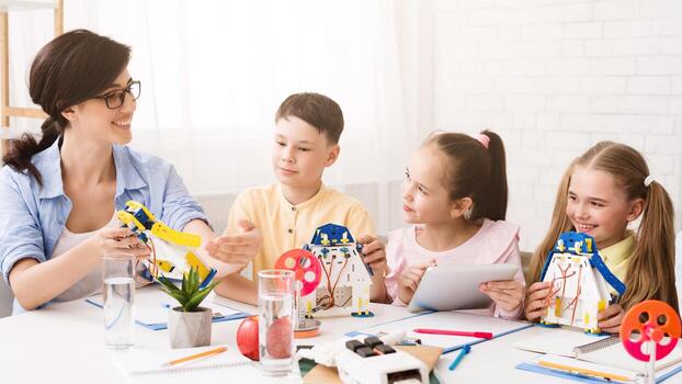 A teacher is showing three students how to build a model robot in a classroom setting. The students are all engaged and interested in the activity. The teacher is pointing to a part of the robot photo