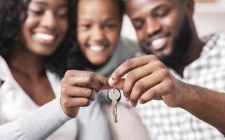Housing concept. Happy black family with daughter holding keys from their new home, selective focus on hands, closeup. photo