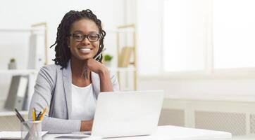 Black woman office worker is typing on her computer in a cubicle. The mood is industrious and efficient, with an organized desk and bright workspace, suggesting productivity. photo