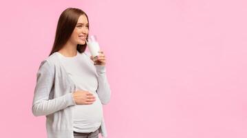 Happy Pregnant Girl Drinking Milk Standing On Gray Studio Background. Dairy Products In Pregnancy. Panorama, Free Space photo