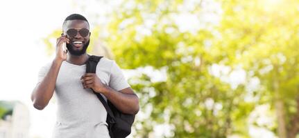 A young man walks through a park while talking on his phone. He is wearing sunglasses and a backpack. photo