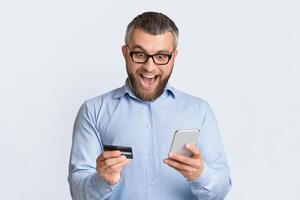 A man is seen holding a smart phone in one hand and a credit card in the other. He appears to be engaged in making a transaction or online purchase using the phone and card. photo