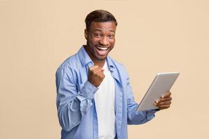 Cheerful African American Guy Holding Digital Tablet Gesturing Yes Standing On Yellow Background. Studio Shot photo