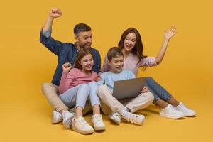 A joyous family consisting of a father, a mother, and two children are sitting together with a laptop, expressing excitement and happiness with raised fists and wide smiles photo