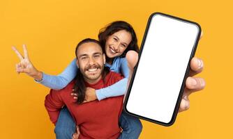 A cheerful man and woman are playfully interacting with each other, with the man holding out a smartphone that has a blank screen suitable for digital mockup photo