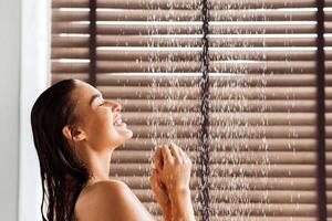 Young woman taking refreshing shower, standing under water drops, side view photo