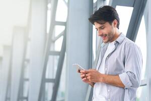 Handsome young guy using smartphone in airport, browsing internet, waiting for the flight, free space photo
