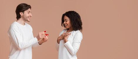 Will You Marry Me. Romantic guy proposing to his surprised girlfriend, giving ring over yellow background with empty space photo