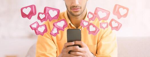 A man sits on a couch, holding a smartphone in his hands, looking down at the screen. A number of pink heart icons, reminiscent of social media notifications, float around him. photo