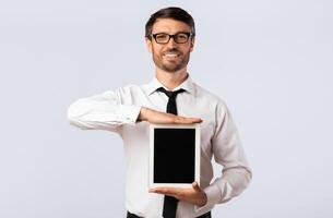Business App. Cheerful Guy Showing Blank Tablet Computer Screen On White Background In Studio. Mockup photo