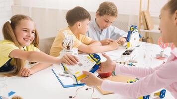 Four students, three girls and one boy, work together to build a robot during a STEM class. The students are all smiling and engaged in the activity, demonstrating their interest in science photo