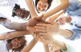 Student Friendship. Portrait of happy university friends stacking hands together, showing unity and togetherness, low angle view, selective focus photo