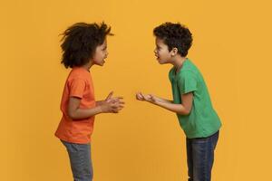 African American young boy and girl are standing face to face with animated expressions, hands gesturing as they appear to be in a playful argument or discussion. photo