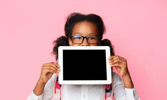 Online School And E-Learning. Schoolgirl Holding Digital Tablet With Blank Screen Recomending Web Classes And Distant Learning On Yellow Background. photo