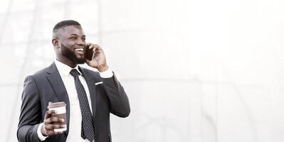 Smiling African American Businessman Chatting On Phone Having Coffee Outdoors In City. Always In Touch Concept. Empty Space photo