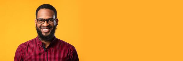 Closeup headshot of content black guy in eyewear looking at camera with smile over yellow studio wall, copy space photo