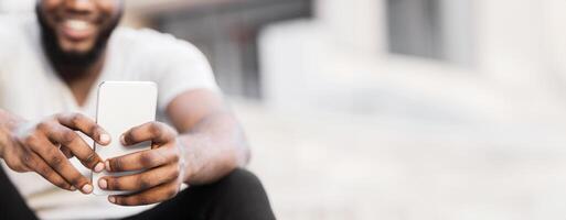 A man with a beard smiles while using a smartphone in a city environment. photo