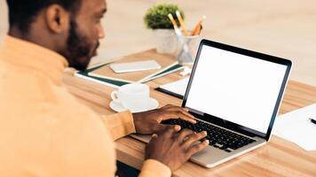 Mock Up Template. Rear view of black man working on laptop with blank screen, typing on keyboard, copyspace photo