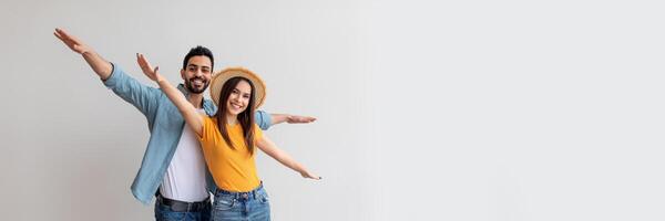 Young couple in love pretending airplane flight, spreading hands like wings, having fun while posing over light studio wall, looking and smiling at camera, copy space photo