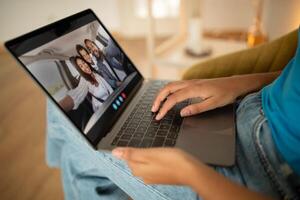 A person is sitting on a couch, using a laptop to chat with a family in a car. The person is using their right hand to navigate the laptop, while their left hand is resting on the laptop photo