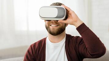 A man with a beard is immersed in virtual reality, wearing a headset that covers his eyes, focused on the virtual experience, with a facial expression reflecting concentration and engagement. photo