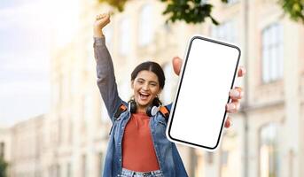 Hindu woman is standing and holding up a smartphone with a blank screen. She is looking at the phone intently, possibly waiting for a response or checking for notifications. photo