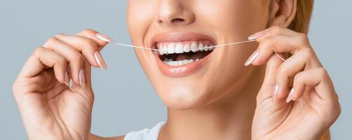 A close-up shot of a woman smiling while flossing her teeth with white floss against a grey background. Her teeth are white and bright, and she is clearly enjoying the process. photo