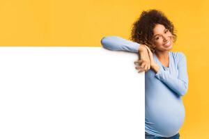 Happy black pregnant woman with empty billboard on light background, copy space photo