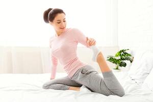 A woman is stretching on a bed with a plant in the background. She is extending her arms and legs in a relaxing manner as she starts her day. photo