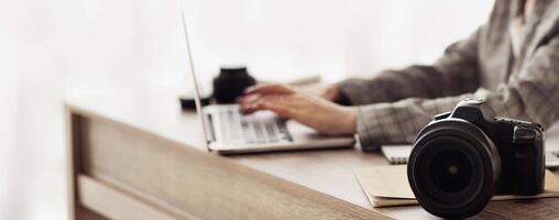 A photographer works on their laptop at a desk, with a camera resting on a notebook in the foreground. photo