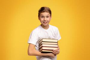 Enjoying remote education. Teen boy smiling with heap of books in hands, orange studio background photo