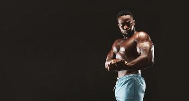 African bodybuilder flexing his muscles, showing biceps in studio, black background photo