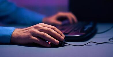 The image shows a closeup of a hand using a computer mouse. The person is sitting in front of a laptop, and the only light in the room is coming from the screen, cropped photo