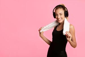 Smiling Fit Girl In Wireless Headphones Listening To Music After Fitness Workout Standing On Yellow Studio Background. Copy Space photo