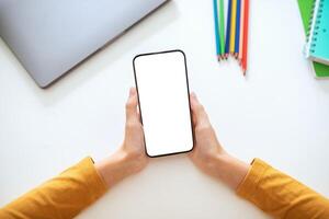 A person is holding a smartphone with a blank screen in their hands. The phone is positioned horizontally, with the screen facing the viewer photo
