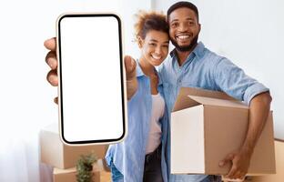 Own House. Happy Black Couple Showing Key Holding Moving Box And Hugging Standing In New Home. photo