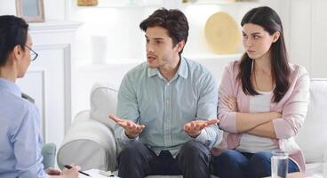 A man and woman are engaged in a counseling session on a couch, conversing with a counselor. They appear focused and attentive as they discuss issues in a calm and professional setting. photo