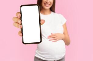 Unrecognizable Pregnant Girl Offering Green Apple To Camera Standing Touching Belly Over White Studio Background. Cropped photo