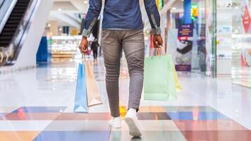 Back view of man is seen walking down a busy mall with multiple shopping bags in hand, possibly enjoying a day of shopping or running errands. photo
